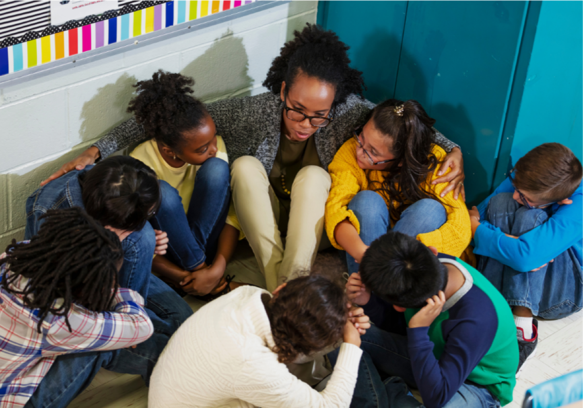 Kids huddle next to their teacher on the floor of their classroom
