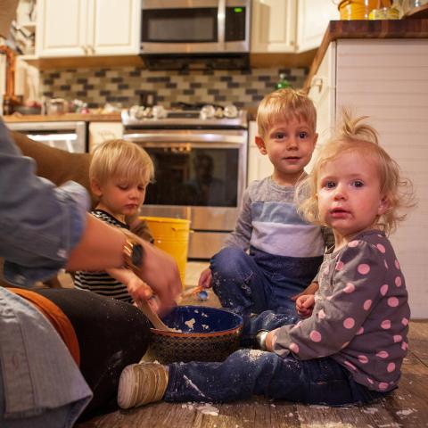 Two little boys and a little girl playing on a kitchen floor