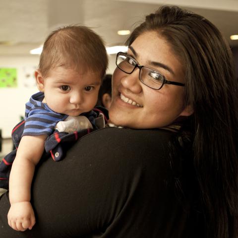 A mom in glasses and a black shirt looking over her left shoulder and holding her one-year-old son