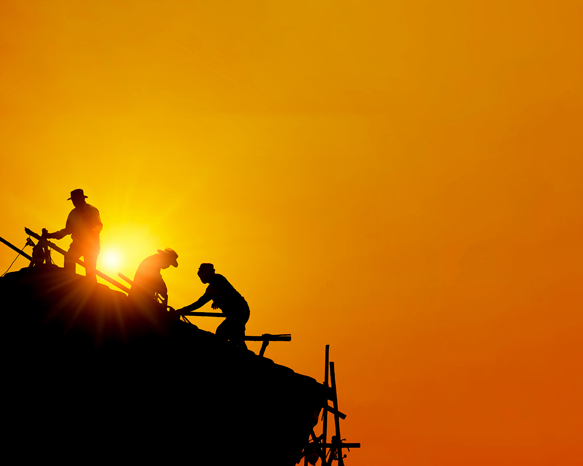 Silhouette of three workers on a roof against the setting sun and an orange sky