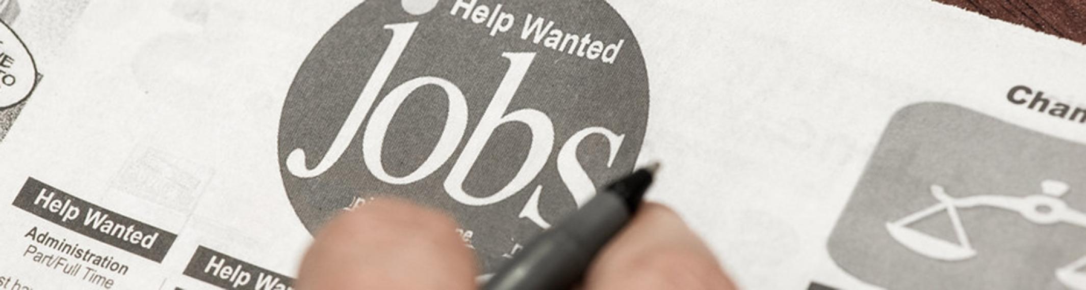 Closeup of two fingers holding a pen over a newspaper's help-wanted section