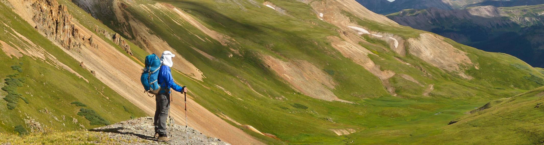 A hiker with poles and a backpack on a mountain vista looks out at the valley below.