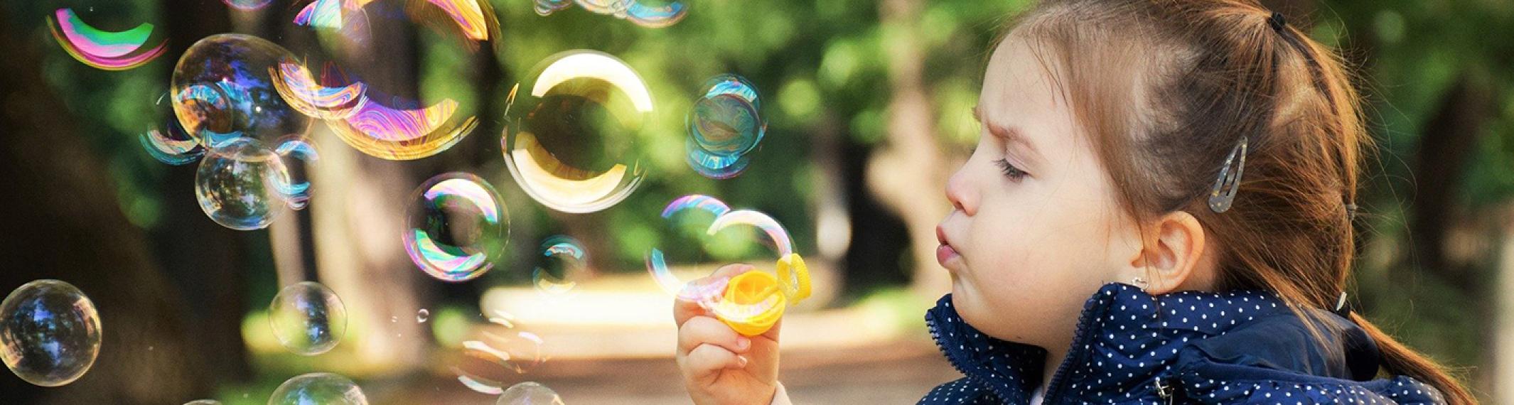 A three year old girl on a path in the tree blowing bubbles