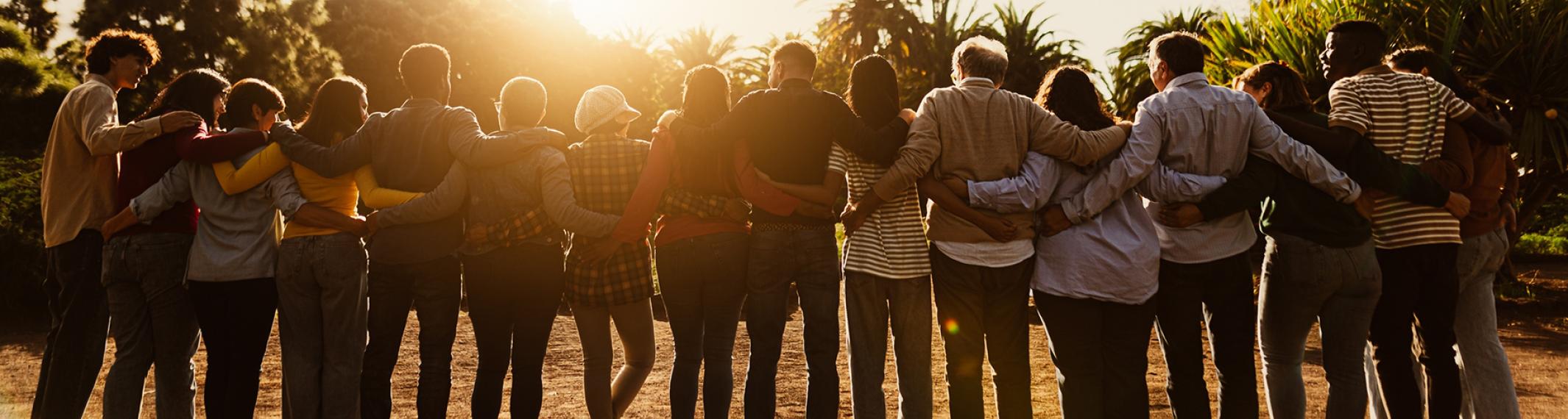 A diverse group of people linking arms at sunset