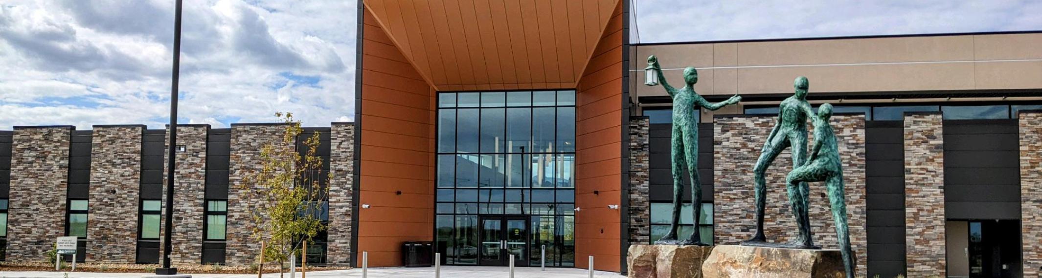 Exterior of Larimer County's Acute Care Behavioral Health facility, with three statues of people helping each other climb onto a rock