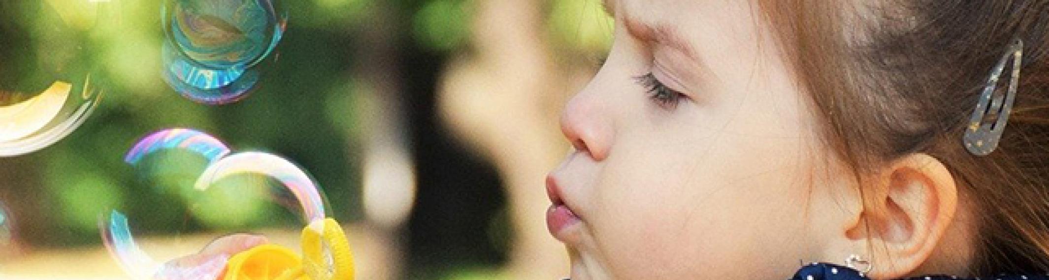 A three year old girl on a path in the tree blowing bubbles