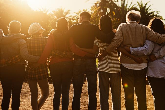A diverse group of people linking arms at sunset