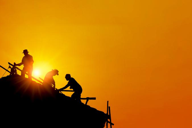 Silhouette of three workers on a roof against the setting sun and an orange sky