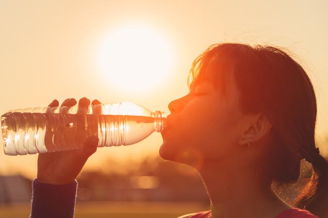 Silhouette of a woman drinking from a water bottle against the sun and an orange sky