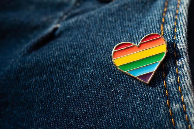 Closeup of blue jeans with a small rainbow-patterned heart pin on the pocket