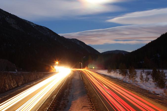 Two lanes of a highway in the mountains at sunset with blurred headlights and taillights