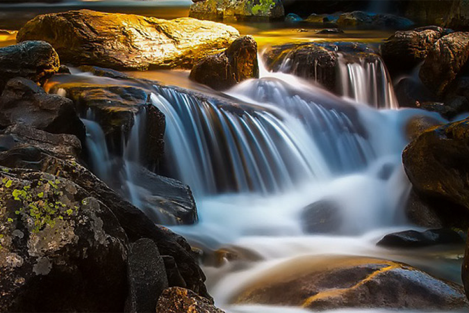 A mountain stream flowing smoothly in a small waterfall over boulders