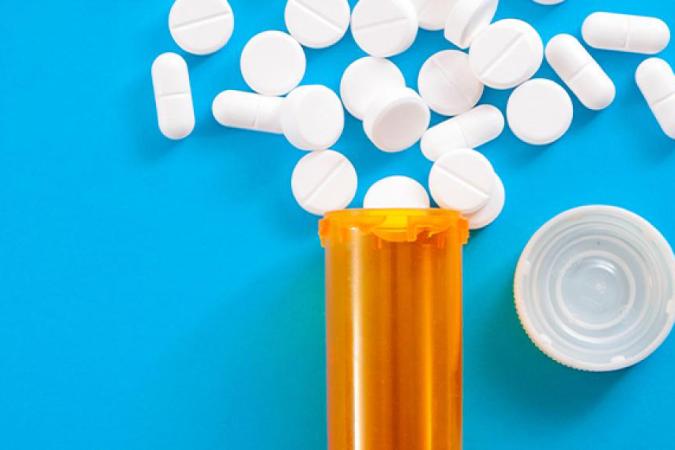 White pills spilling out of an orange bottle onto a light blue background