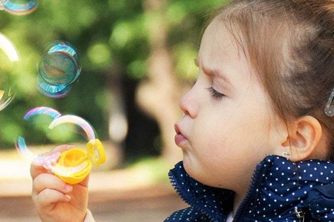 A three year old girl on a path in the tree blowing bubbles