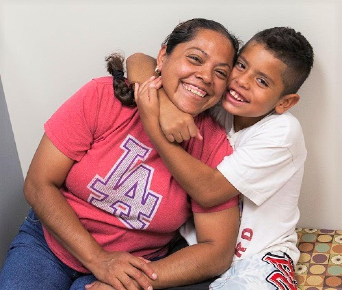 Boy gives his mom a side hug around her neck, pulling her toward him