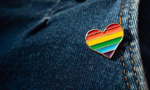 Closeup of blue jeans with a small rainbow-patterned heart pin on the pocket