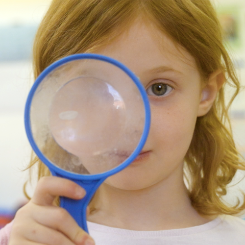 A preschool girl looking through a magnifying glass